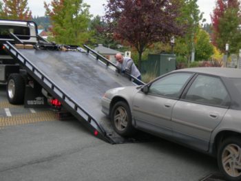 A man with his towing truck setting up to tow a gray car