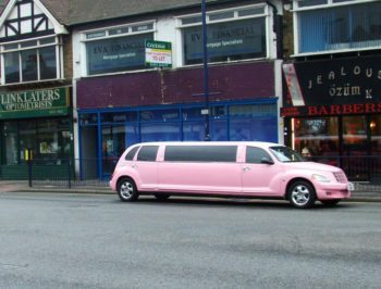 A pink limousine parked in front of a barbershop