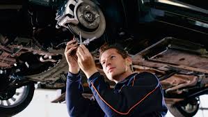 A man standing in a lifted car fixing the front brake