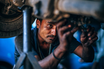 A man underneath a lifted car fixing the engine